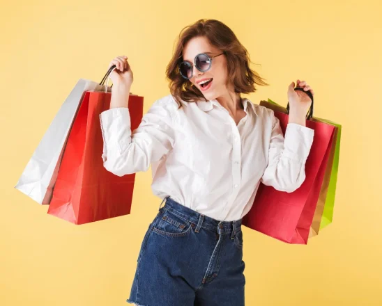 portrait-happy-lady-sunglasses-standing-with-colorful-shopping-bags-hands-pink-background-young-woman-standing-white-shirt-denim-shorts